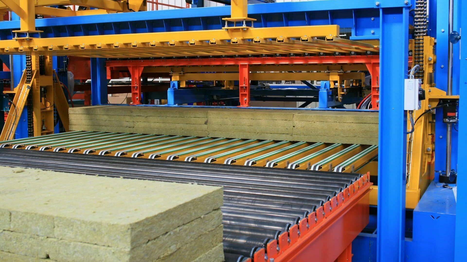 Empileur de panneaux isolants alimenté par un convoyeur à rouleaux
