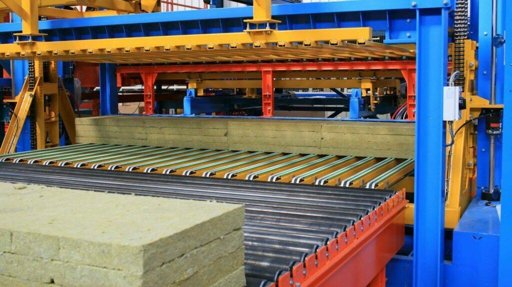 Empileur de panneaux isolants alimenté par un convoyeur à rouleaux